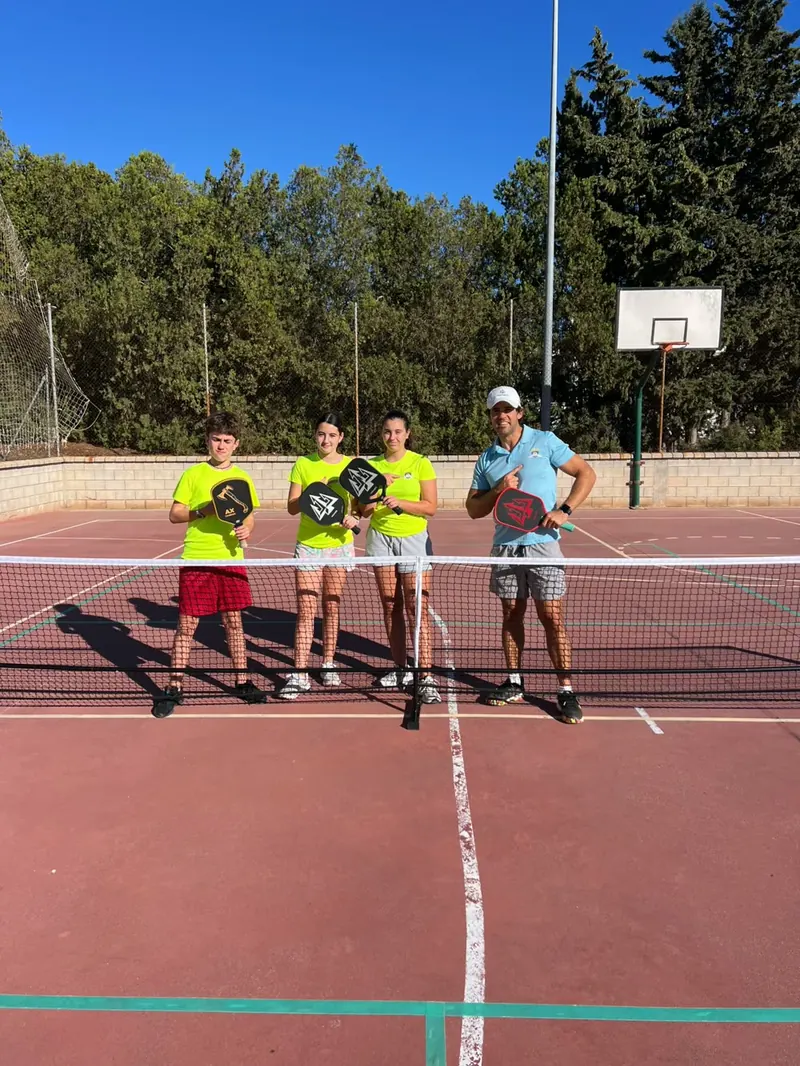 Entrenador con tres niños y palas de pickleball en la pista